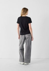 T-shirt in cotone nero con maniche corte, abbinato a jeans grigi chiari e larghi. Calzature casual completano l'outfit.