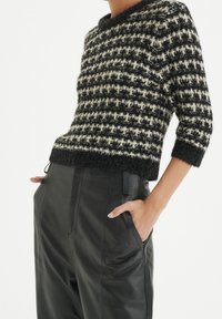 Pull court à carreaux noir et crème avec une texture duveteuse et un col rond, associé à un pantalon en cuir noir taille haute.