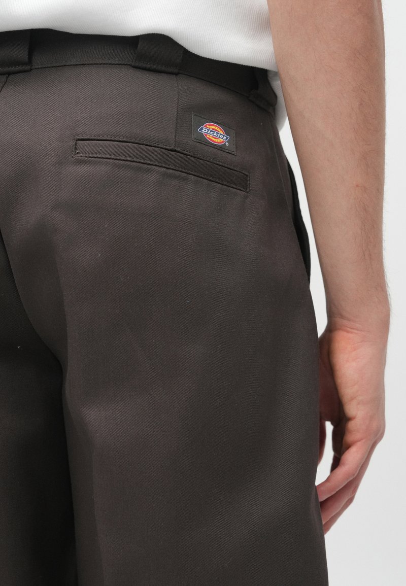 Mørkebrune bukser lavet af kraftigt stof, med en baglomme og et rektangulært Dickies-logo-patch på bagsiden.
