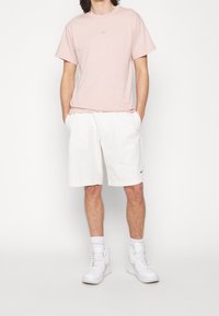 Ljust rosa bomullströja med en liten vit logga, kombinerad med vita veckade shorts och vita högstövlar. En enkel och avslappnad outfit.