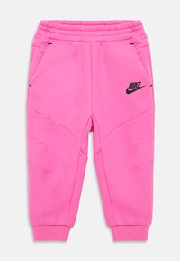 Różowe spodnie dresowe wykonane z miękkiego materiału, z czarnym logo Nike i kieszeniami bocznymi, mają ściągacze przy nogawkach i luźny krój.