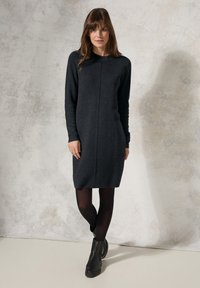Abito lavorato a maglia grigio scuro con maniche lunghe, collo alto e una forma leggermente strutturata, abbinato a stivaletti neri e collant.