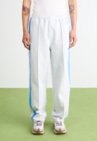 White sweatpants with blue side stripes and zipper pockets. Made of smooth fabric, featuring a relaxed fit and tapered legs.