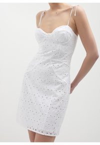 Robe blanche en coton brodé, avec un corsage ajusté, des bretelles spaghetti et des motifs floraux découpés sur toute la jupe.