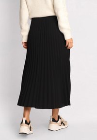 Sort plisseret midi-skjorte med ribbet tekstur, parret med en cremet sweater og beige sneakers, der viser en afslappet pasform og en flydende silhuet.