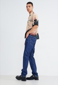 Majica s kratkimi rokavi z abstraktnimi bež, črnimi in modrimi vzorci oblakov; modri jeans; črne čevlje; preprost, sproščen dizajn.