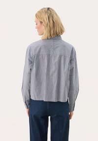 W paski, krótką bluzkę z szarej i białej bawełny z detalem na plecach i długimi rękawami. Stylizowana z ciemnoniebieskimi spodniami dżinsowymi.