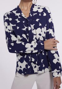 Blouse bleu marine avec un motif floral abstrait blanc, à manches longues et décolleté en V. Conçue en tissu léger et avec une coupe légèrement ample.
