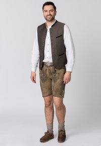 Braune Lederhosen mit aufwendiger Stickerei, kombiniert mit einer dunkel gemusterten Weste über einem weißen Hemd. Braune Schnürschuhe und graue Kniestrümpfe.