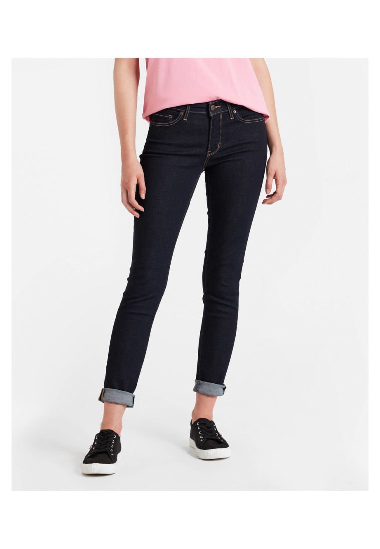 Jeans de mezclilla azul oscuro con un corte slim, puños enrollados y costuras en contraste. Combinados con zapatillas negras y una blusa rosa.