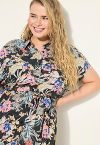 Blumenkleid aus schwarzem Stoff mit bunten Mustern, kurzen Ärmeln, Knopfleiste und gebundenem Taillendetail.
