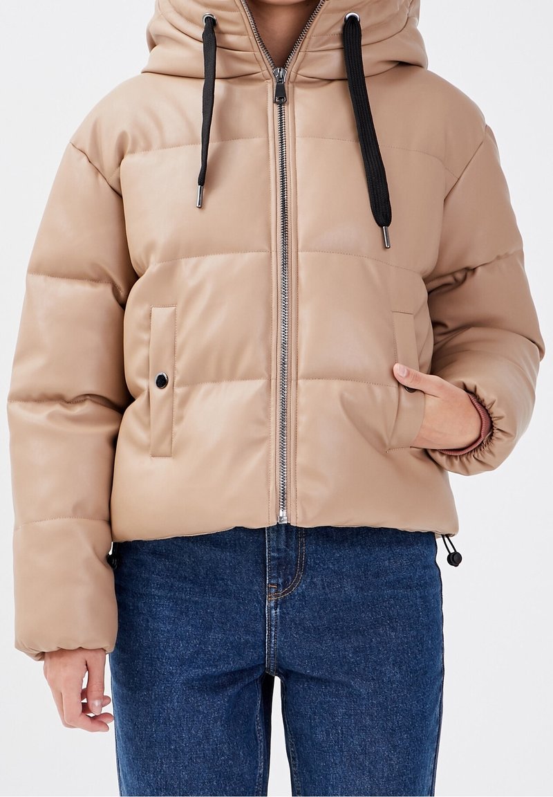 Doudoune beige avec capuche, fermeture éclair sur le devant et cordons noirs. Caractéristiques : design matelassé et poche latérale avec fermeture à pression.