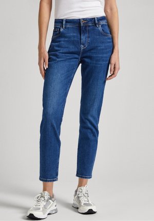 Blå denimjeans med en figursydd passform, medelhög midja, femficksdesign och vävda detaljer, tillsammans med grå och vita sneakers.