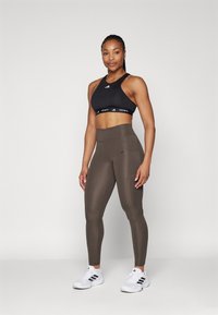 Black sports bra and olive green high-waisted leggings, both made from stretchy material, with Adidas logos and a side pocket on the leggings.
