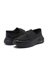 Paar schwarze Freizeitschuhe mit Wildlederobermaterial, Schnürverschluss, dicken strukturierten Gummisohlen und Vibram-Logo an der Seite.