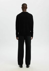 Černý svetr s kulatým výstřihem a vroubkovanými manžetami, zkombinovaný s volně střiženými černými kalhotami. Hladká textura; minimalistický design.