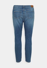 Chude dżinsy w średnim niebieskim deni, z dwoma tylnymi kieszeniami, średnim stanem i skórzaną łatką na pasku.