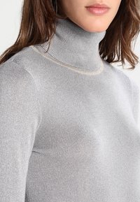 Silberner Rollkragenpullover aus geripptem Stoff mit subtiler Sheen-Oberfläche. Verfügt über ein figurbetontes Design und einen hohen Kragen mit dezenten Akzenten in der Naht.