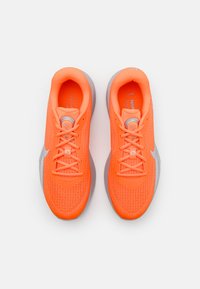 Šviesiai oranžiniai sportiniai bateliai su tekstūruotu audiniu, apvaliais raišteliais, sidabriniais akcentais ir paminkštintu pilku padu.