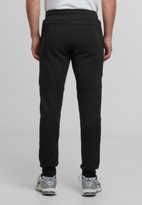 Svarta sweatpants med strukturerad yta, elastisk midjeband och skräddarsydd passform. Har knäpaneler och sidofickor. Bärs med grå sneakers.