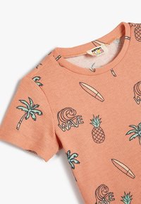 Persikofärgad ribbad t-shirt med kort ärm som har gröna palmer, surfbrädor, ananaser och texten "WAVE" tryckt i svart.