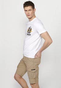 White cotton t-shirt with graphic design on the front, paired with beige cargo shorts featuring pockets and stitching details.