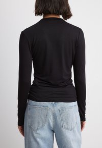 Maglietta nera a maniche lunghe con design aderente, texture liscia e scollatura rotonda, abbinata a jeans in denim azzurro chiaro a vita alta.