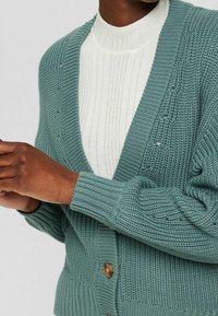 Sweter kardigan w odcieniu zielono-niebieskim z dekoltem w serek i prążkowanymi mankietami, z subtelnymi detalami i centralnym zapięciem na guzik. Nosić na białej bluzce prążkowanej.