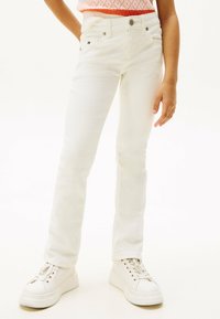 Weiße Jeans im Slim-Fit-Stil mit fünf Taschen, einem Knopfverschluss und dezenten Markenakzenten. Getragen mit weißen Sneakers.