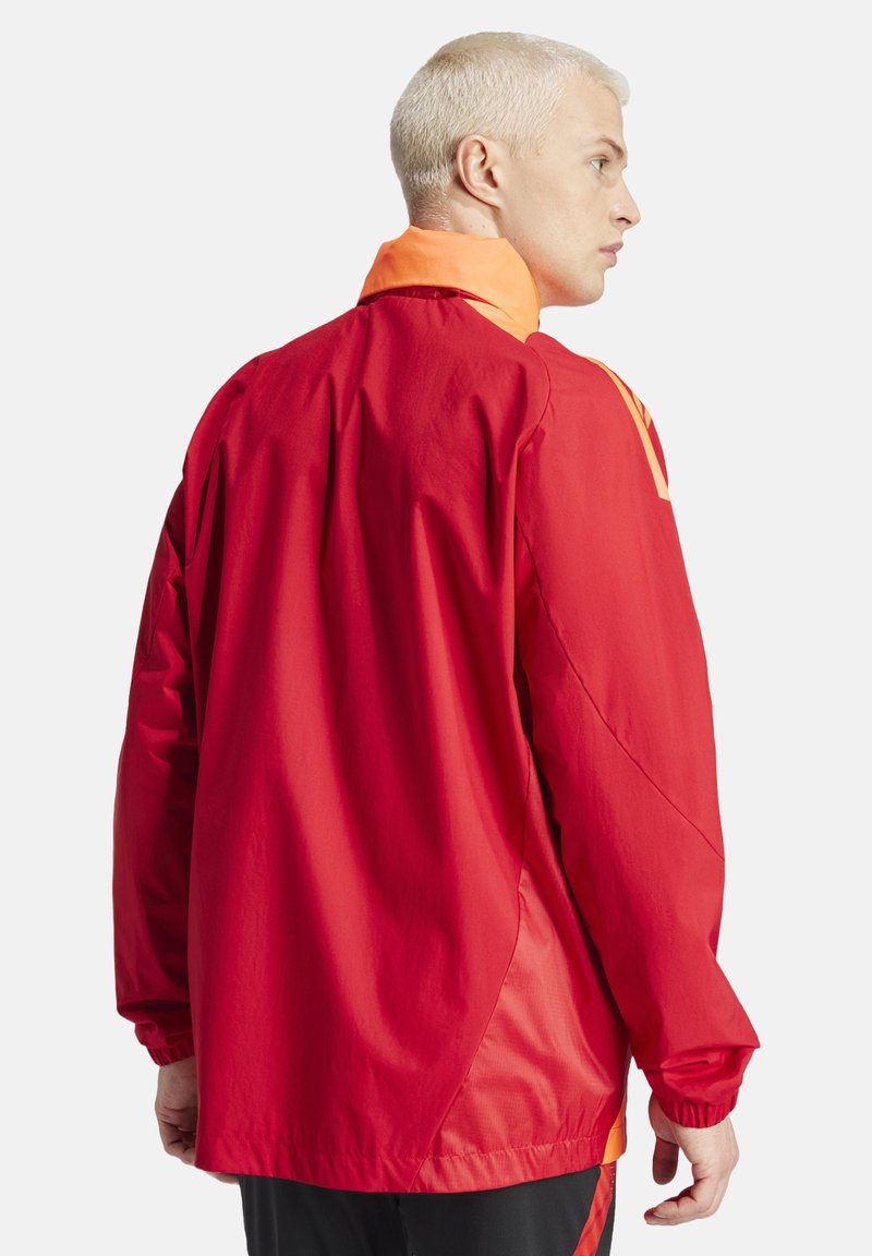 Red windbreaker jacket with an orange collar. Features long sleeves, elastic cuffs, and a relaxed fit. Material appears lightweight and smooth.