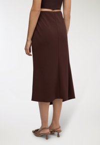 Gonna marrone di lunghezza media, realizzata in tessuto liscio, con design svasato e cucitura posteriore sottile. Abbinata a sandali marroni con tacco.