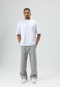 T-shirt en coton blanc à manches courtes associé à un pantalon de survêtement gris avec cordon de serrage. Le mannequin porte des baskets blanches. Design simple.