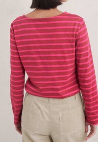 Långärmad topp i röd med ljusrosa horisontella ränder. I bomullstyg, rund halsringning och avslappnad passform. Bärs med ljusbeige kordflöjlsbyxor.