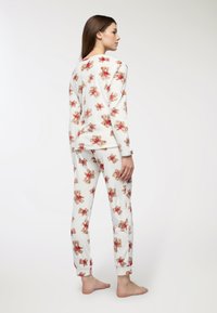 Set di pigiama bianco in cotone con motivo di orsetti marroni e rossi. Presenta maniche lunghe e pantaloni aderenti con polsini elastici alle caviglie.