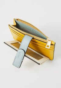 Portafoglio in pelle gialla con una tracolla azzurro chiaro, chiusura a zip e molteplici scomparti per carte. Texture liscia e dettagli in metallo dorato.