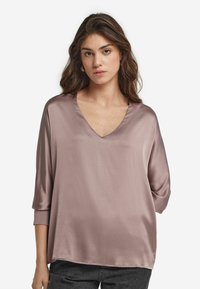 Satinbluse in Mauve, mit V-Ausschnitt, trois-quart-Ärmeln und lockerer Passform. Glatte Textur mit minimalen Nähten.