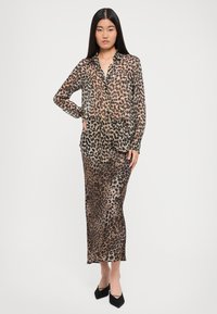 Leopardmønster skjorte og maxiskjørt i gjennomsiktig stoff. Brune og svarte flekker på en beige bakgrunn. Lange ermer og knappestyling foran.