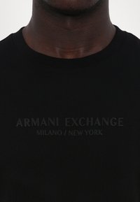 Schwarzes Rundhals-T-Shirt aus samtiger Baumwolle. Verfügt über erhabenen Text "ARMANI EXCHANGE MILANO / NEW YORK" über der Brust.
