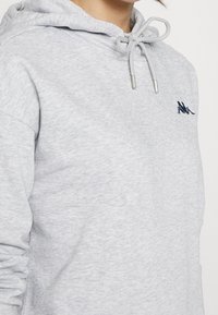 Sweat à capuche gris clair en tissu doux avec fermeture à cordon et logo brodé en bleu marine. Dispose d'une poche kangourou.