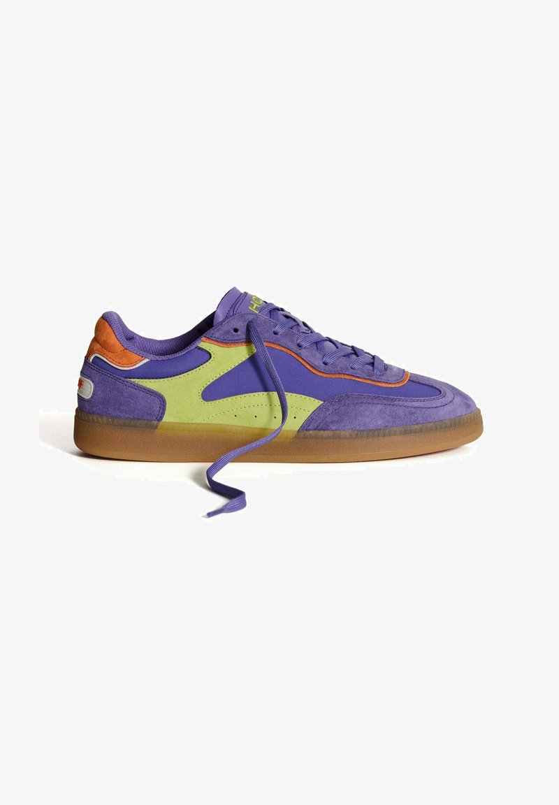Zapatilla púrpura con acentos en verde y naranja, materiales de ante y sintéticos, suela de goma, cordones planos y diseño de puntera redonda.