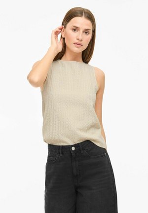 Top sin mangas beige con un patrón texturizado, combinado con jeans negros de cintura alta. Diseño simple con escote redondo.