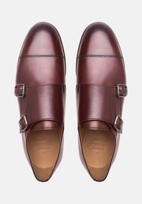 Une paire de chaussures de ville en cuir brun poli, à double boucle, vue du dessus sur un fond blanc.