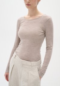 Maglietta a maniche lunghe color tortora realizzata in un tessuto testurizzato, abbinata a pantaloni in lino beige chiaro a vita alta con frontale piatto e tasche.