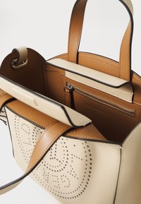 Leren handtas in tan en crème met geperforeerd ontwerp. Heeft twee handvatten aan de bovenkant, een ritssluiting binnenzak en een gestructureerde vorm.