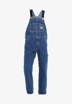 Dżinsowe ogrodniczki w średnim niebieskim odcieniu, z regulowanymi czarnymi ramiączkami, wieloma kieszeniami i metalowymi akcentami.