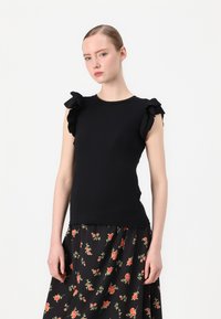 Top nero a maniche corte con dettagli a volant sulle spalle, caratterizzato da una vestibilità aderente e una texture morbida, abbinato a una gonna con motivo floreale.