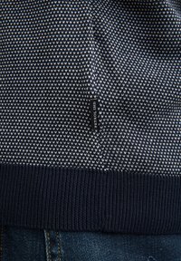 Maglione blu navy con motivo geometrico bianco, presenta una scollatura e un'orlo a coste. È visibile un'etichetta nera con la scritta "PETROL IND".