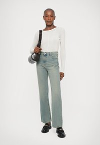 Top blanco de manga larga, jeans de tiro alto azul claro y mocasines negros. Bolso pequeño redondo texturizado con una correa corta.
