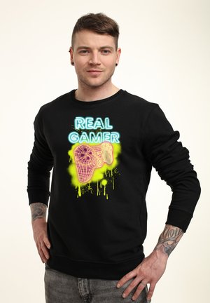 Sort sweatshirt med et neongrafik af en spilkonsol og teksten "REAL GAMER" i blå og grøn splatter-accenter.