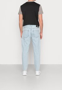 Svart och grå kortärmad skjorta som bärs tillsammans med ljusblå denimjeans. Jeansen har en avslappnad passform och har en CK-logotyp på baksidan.